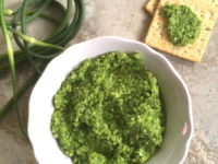 green garlic scape pesto in a bowl with crackers nearby