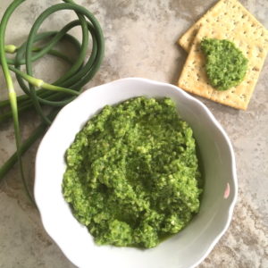 green garlic scape pesto in a bowl with crackers nearby